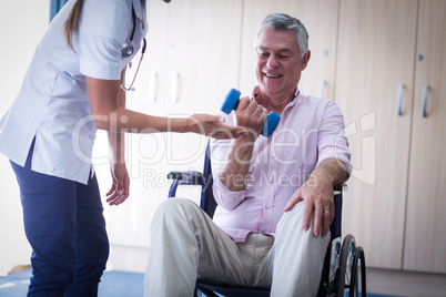 Female doctor assisting senior man in lifting dumbbell