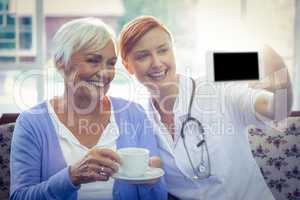 Smiling doctor and patient looking at phone while having tea