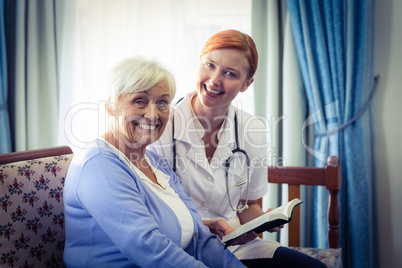Smiling doctor helping senior woman to read a book