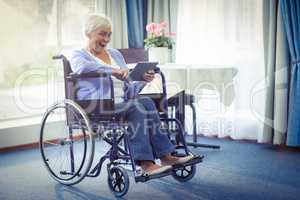 Excited senior woman on wheelchair using digital tablet