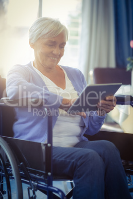 Happy senior woman on wheelchair using digital tablet