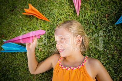 Young girl lying on grass around paper planes