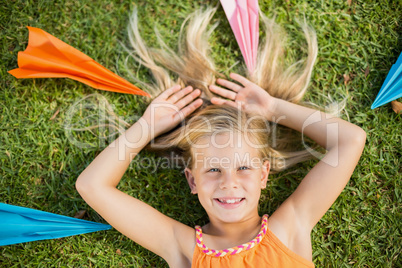Young girl lying on grass around paper planes