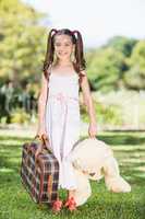 Young girl holding a suitcase and teddy bear