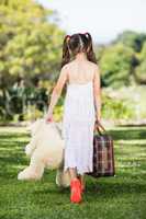 Young girl walking in park with a suitcase and teddy bear