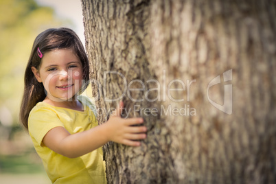 Smiling girl hugging  tree trunk in park