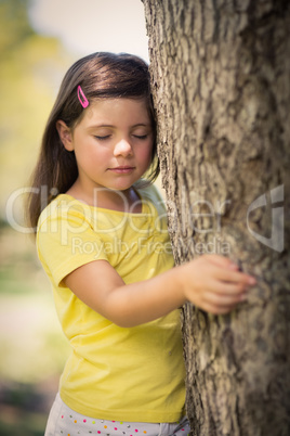 Thoughtful girl leaning on tree trunk