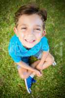 Young boy sitting on grass and smiling at camera in park