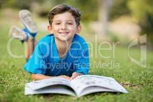 Young boy lying on grass with book