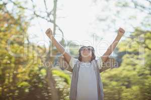 Excited boy standing in park with arms raised