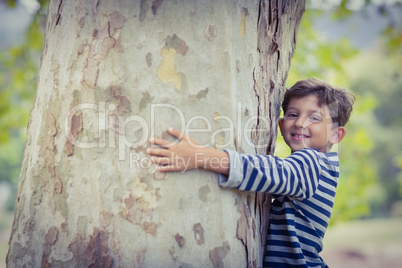 Smiling boy hugging tree trunk in park