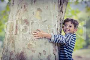 Smiling boy hugging tree trunk in park
