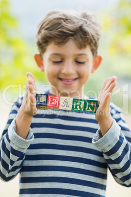 Boy holding blocks in park which reads learn