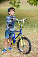 Smiling boy standing with bicycle in park