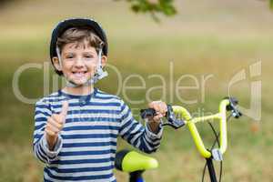 Boy showing his thumbs up standing next to bicycle
