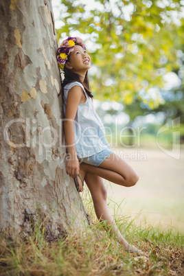 Thoughtful girl leaning on tree trunk in park