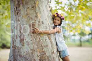 Portrait of smiling girl hugging tree trunk in park