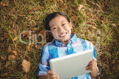 Portrait of smiling girl lying on grass and using digital tablet