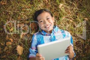 Portrait of smiling girl lying on grass and using digital tablet