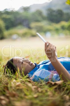 Smiling girl lying on grass and using digital tablet