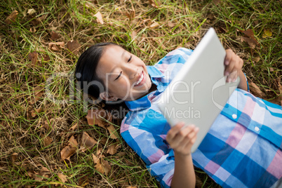 Smiling girl lying on grass and using digital tablet