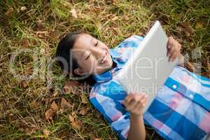 Smiling girl lying on grass and using digital tablet