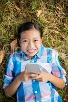 Portrait of smiling Girl lying on grass and using mobile phone