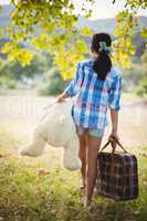 Girl walking in park with a suitcase and teddy bear