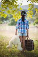 Girl standing in the park with a teddy bear and suitcases
