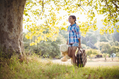 Girl walking in park with a suitcase and teddy bear