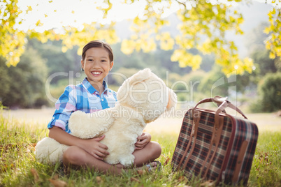 Young girl sitting with a teddy bear and suitcase