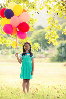 Portrait of smiling girl holding balloons in park