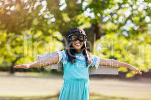 Smiling girl standing with arms outstretched in park