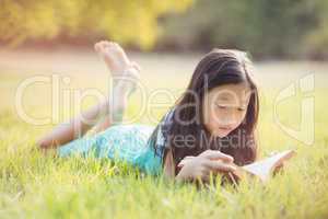 Young girl lying on grass and reading book in park