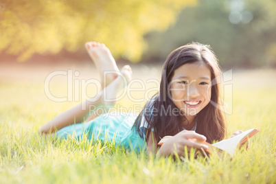 Portrait of smiling girl lying on grass and reading book in park