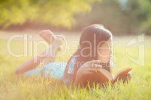 Thoughtful girl lying on grass and reading book in park