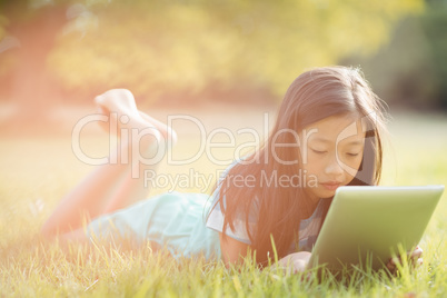 Girl lying on grass and using digital tablet in park