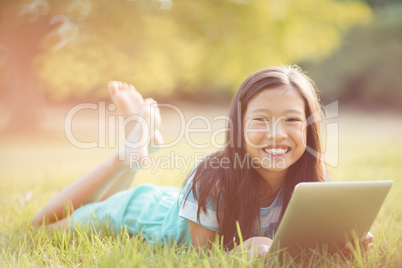 Portrait of smiling girl lying on grass and using digital tablet