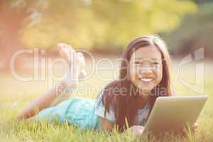 Portrait of smiling girl lying on grass and using digital tablet