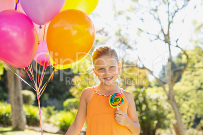 Portrait of smiling girl holding balloons and lollypop in the park