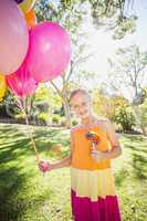 Portrait of smiling girl holding balloons and lollypop in the park