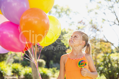 Smiling girl holding balloons and lollypop in the park