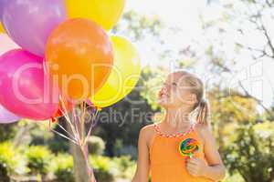 Smiling girl holding balloons and lollypop in the park