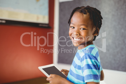 Portrait of schoolboy holding digital tablet in classroom