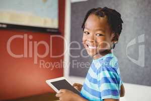 Portrait of schoolboy holding digital tablet in classroom