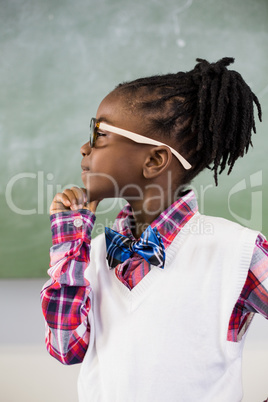 Thoughtful schoolgirl standing with hand on chin in classroom