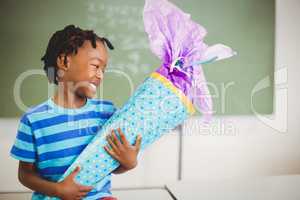Happy schoolboy holding gift in classroom