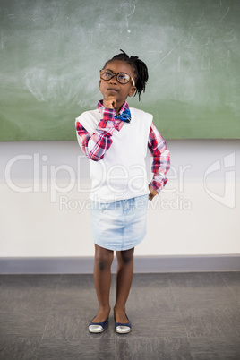 Thoughtful schoolgirl standing with hand on chin in classroom