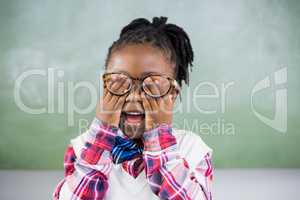 Smiling schoolgirl covering her eyes in classroom