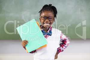 Portrait of happy schoolgirl holding file in classroom